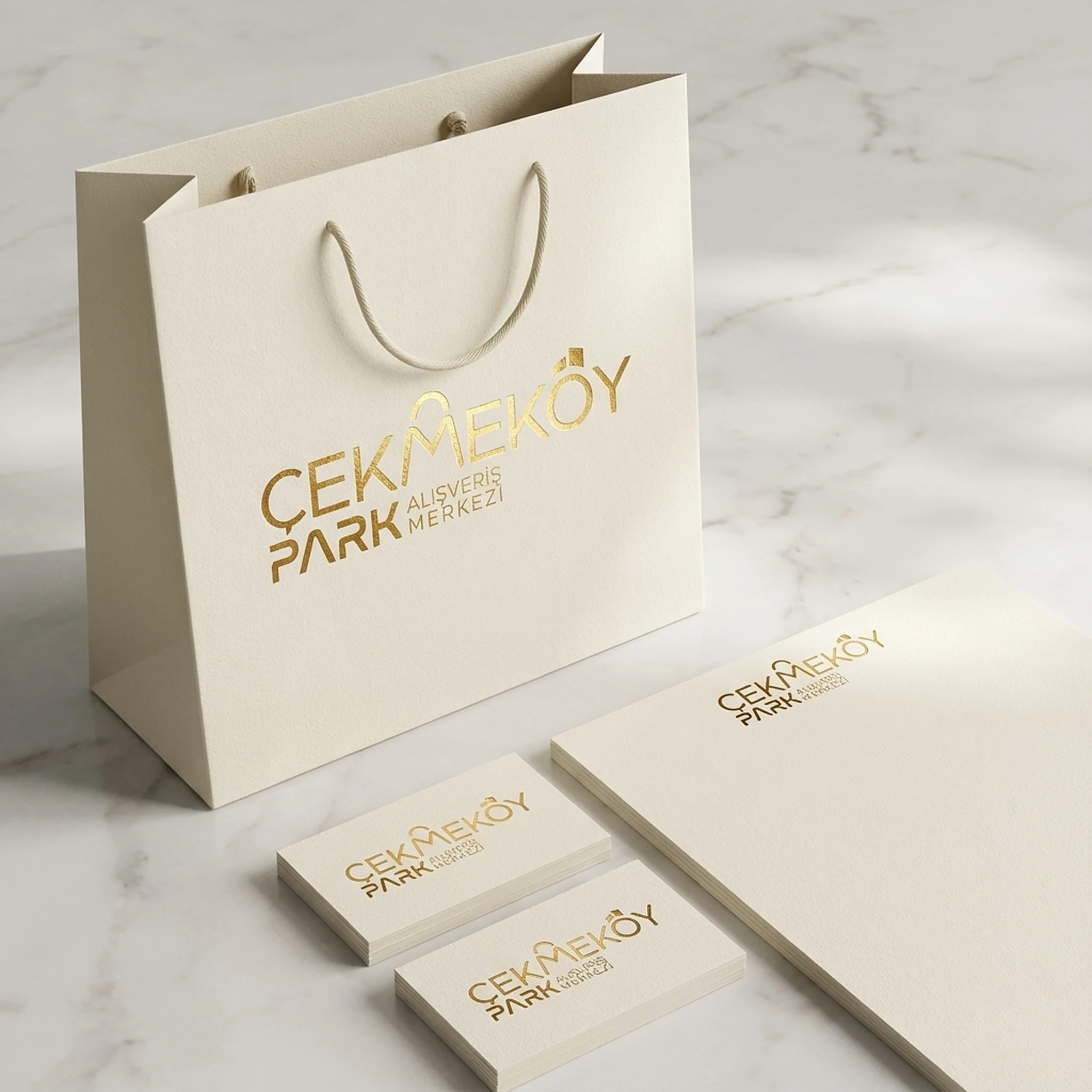 Krem renkli alışveriş çantası, kartvizit ve not kâğıdı üzerinde altın renkli logo, mockup